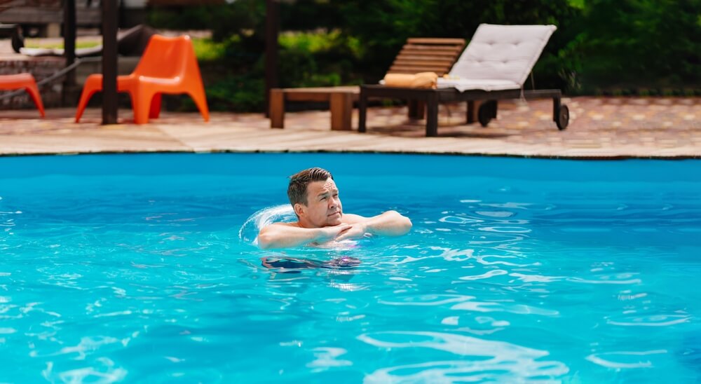 Portrait of a cheerful middle-aged man in the pool with inflatable lifebuoy.