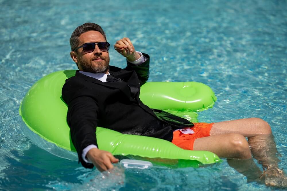 Funny business man in a business suit works for a laptop standing in the water in pool